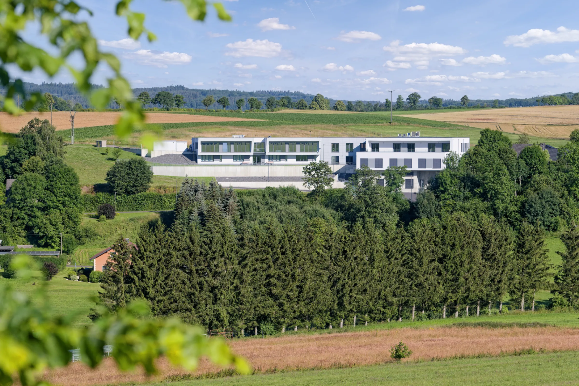 The image shows the Premosys headquarter, completed in 2023, situated in the scenic Vulkaneifel region. The modern facility houses its own technical center, research and development department, automation division, and extensive production areas.