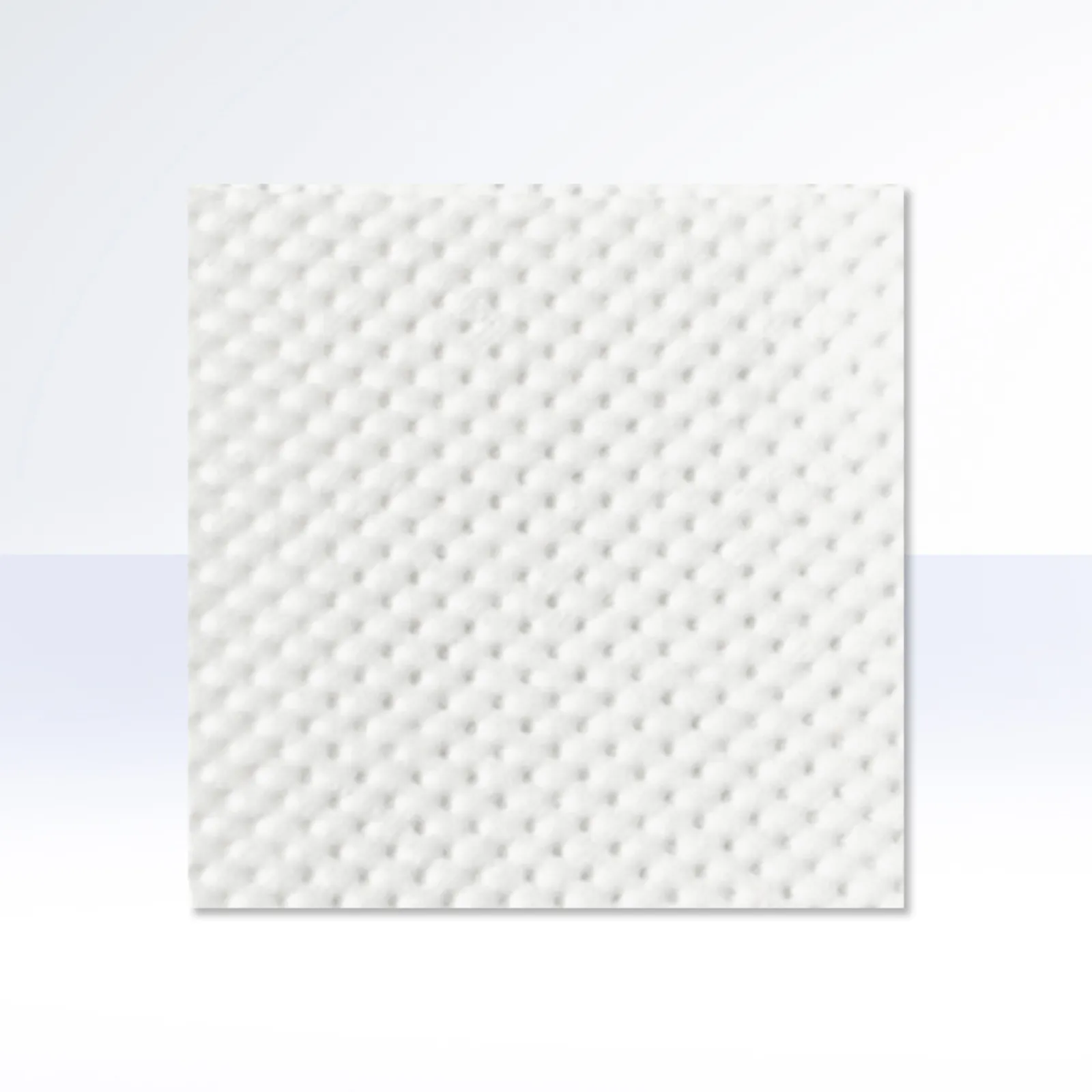 Close-up of a white DEBAMED® absorbent pad with a uniform dimpled texture, shown against a soft white-to-light-blue gradient background.
